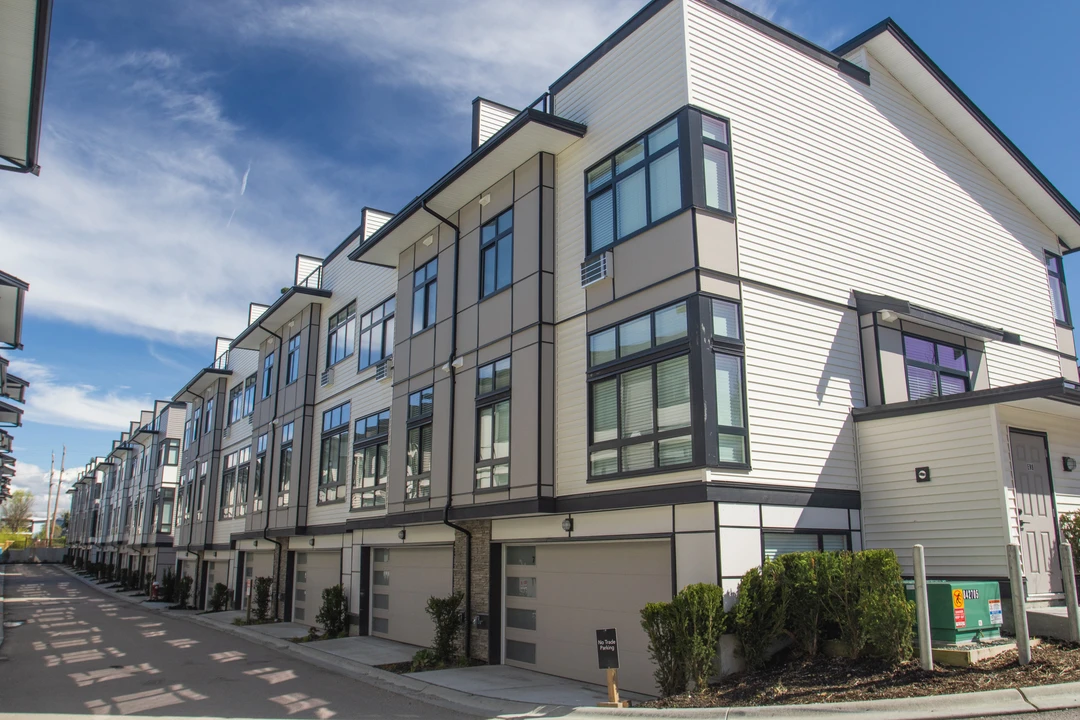 Row of modern townhomes with large windows and garage doors, set against a bright blue sky dotted with clouds.
